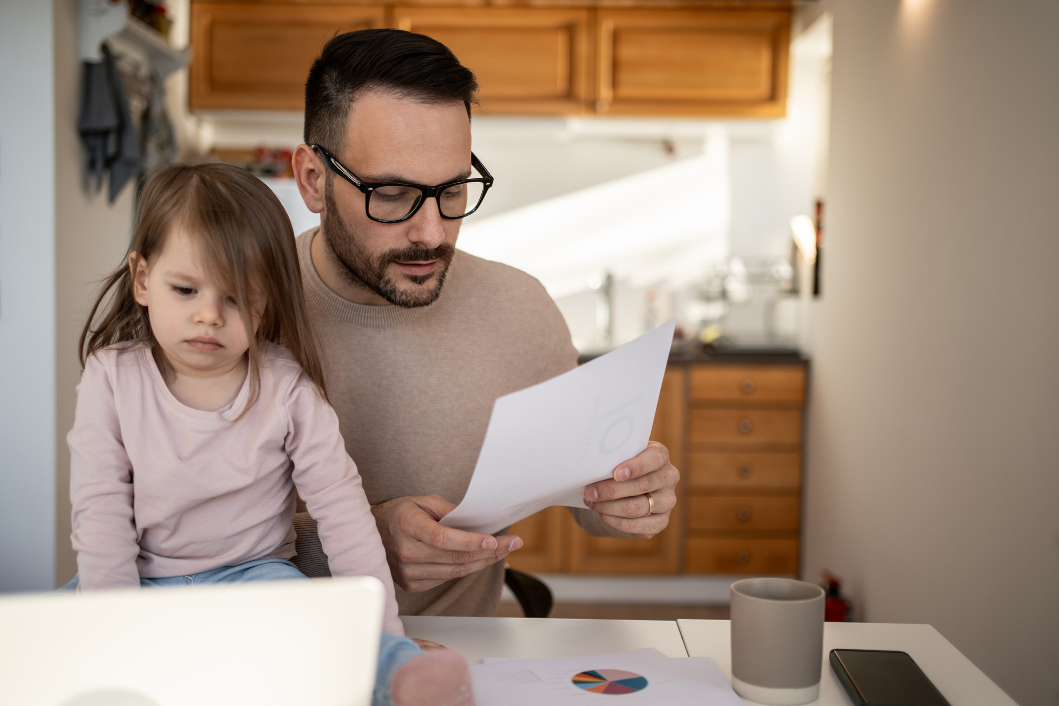 A father calculating the cost of childcare and child support with his daughter nearby
